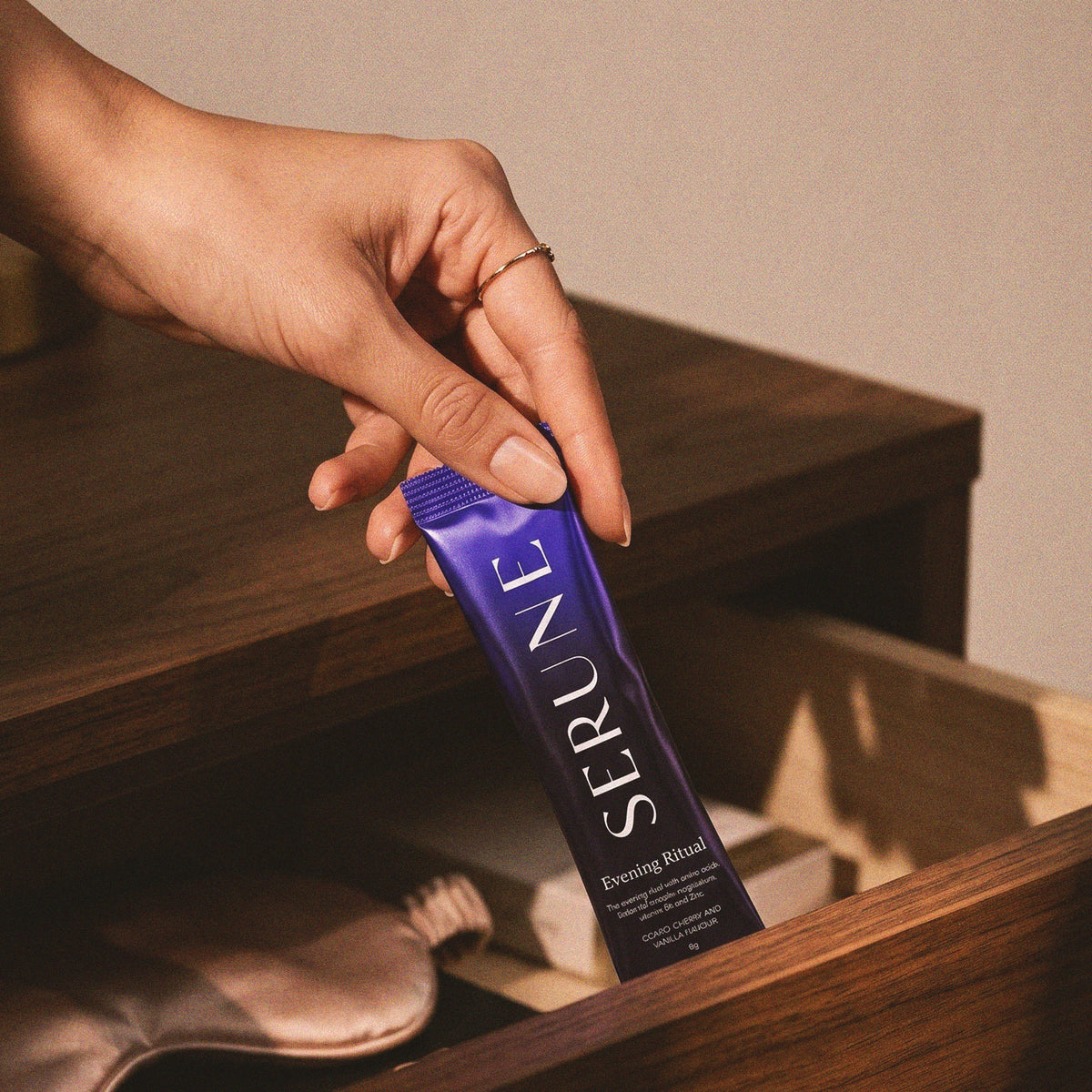 A hand taking a Serune sachet from a bedside drawer